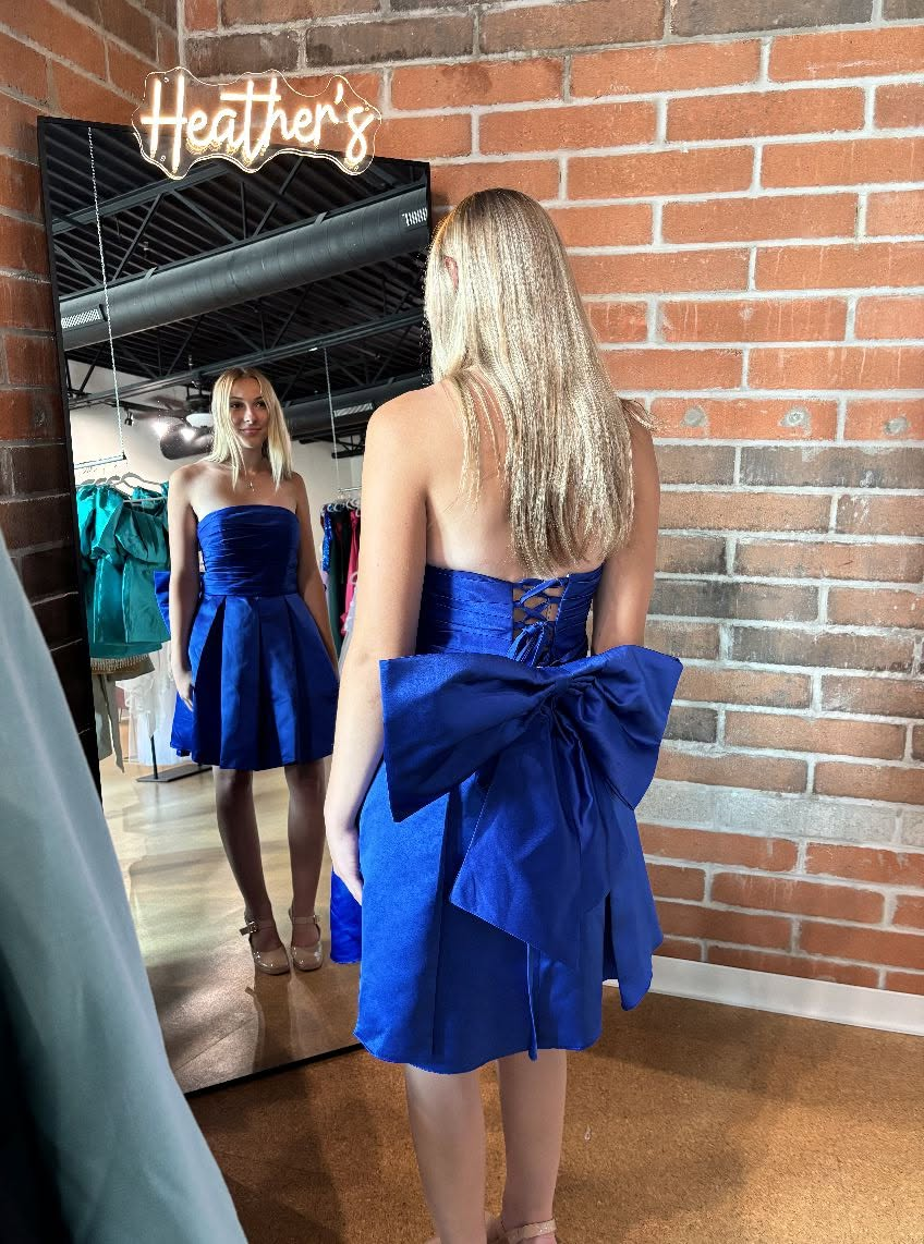 A student trying on a royal blue prom dress in front of a full-length mirror below the Heather's Boutique neon sign